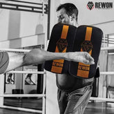 Rewon black and golden MMA training pads in action during an intense kickboxing session in a gym setting, highlighting durability and protection.